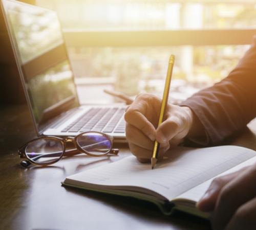 Person writing with laptop open.