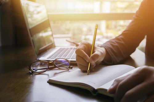Person writing with laptop open.
