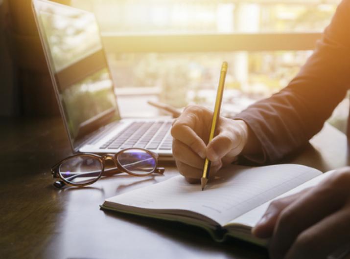 Person writing with laptop open.